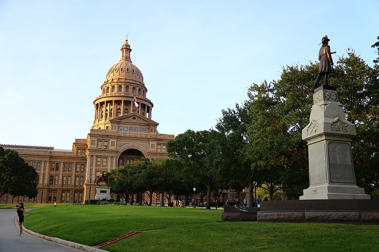 Texas State Capitol dome and front lawn in Austin, with a monument at right.